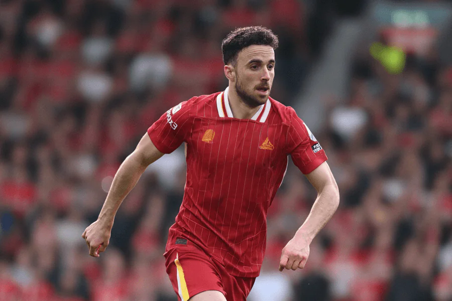 Diogo Jota célébrant un but décisif sous le maillot de Liverpool, pointant le ciel en hommage à ses supporters au stade d’Anfield.